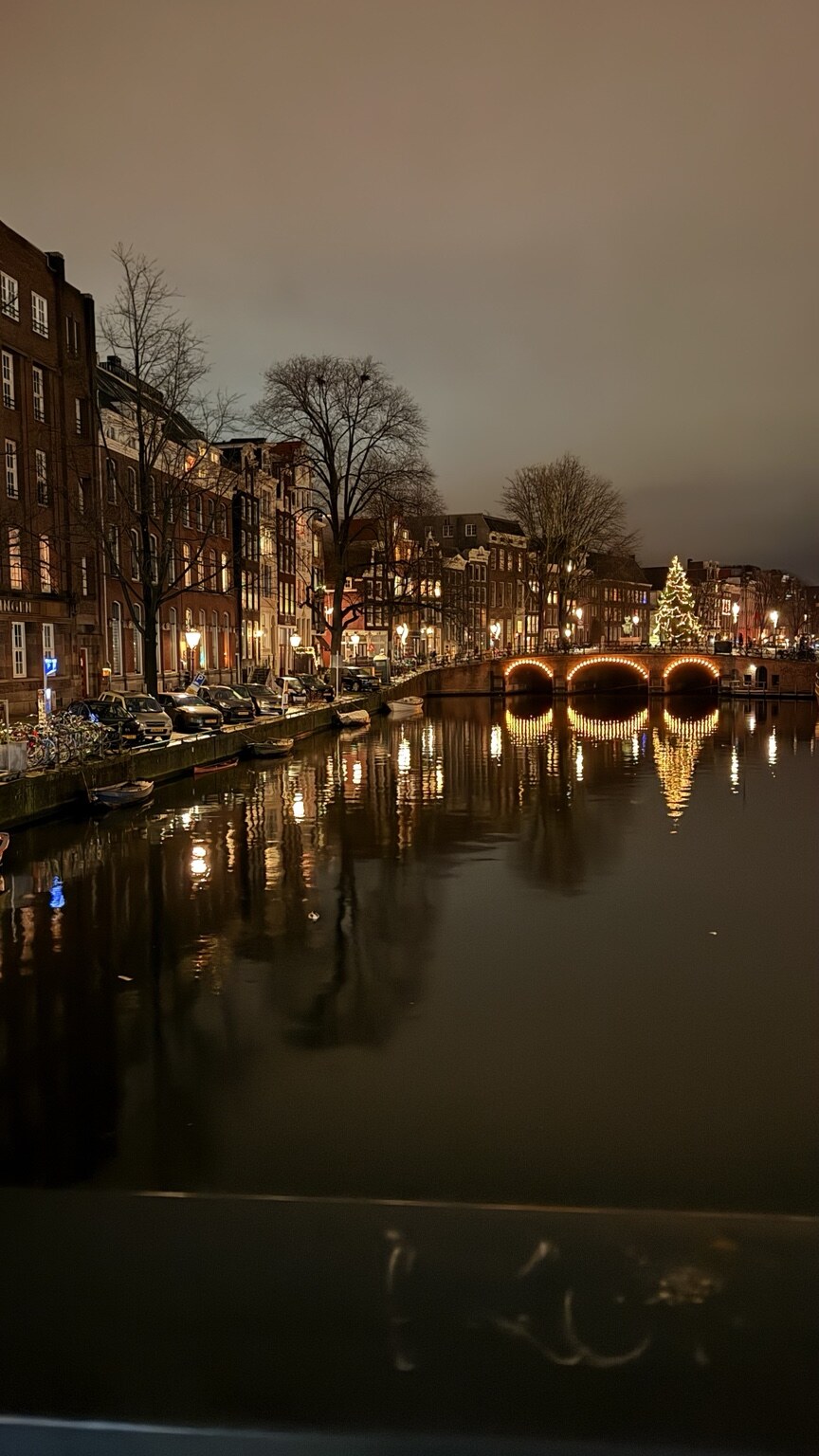 Amsterdam canal at night with bridge lights reflected in the water