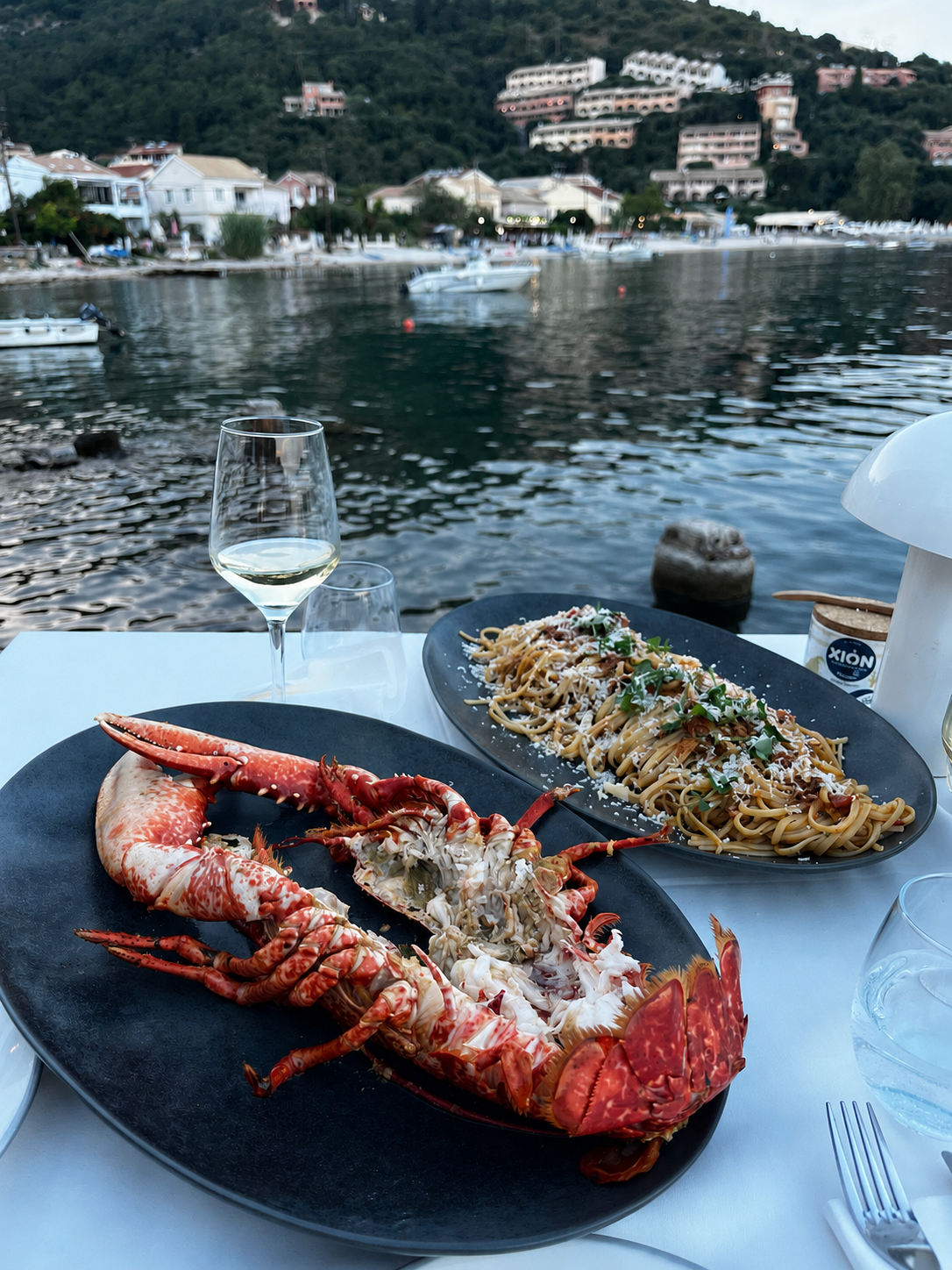 A whole lobster on a black plate with Kalami Bay behind it in daylight