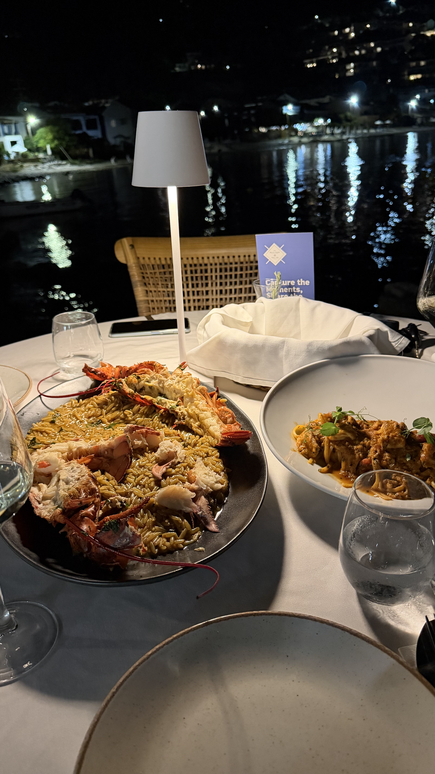An evening table on the water with lobster orzo and shrimp pasta lit by a small lamp